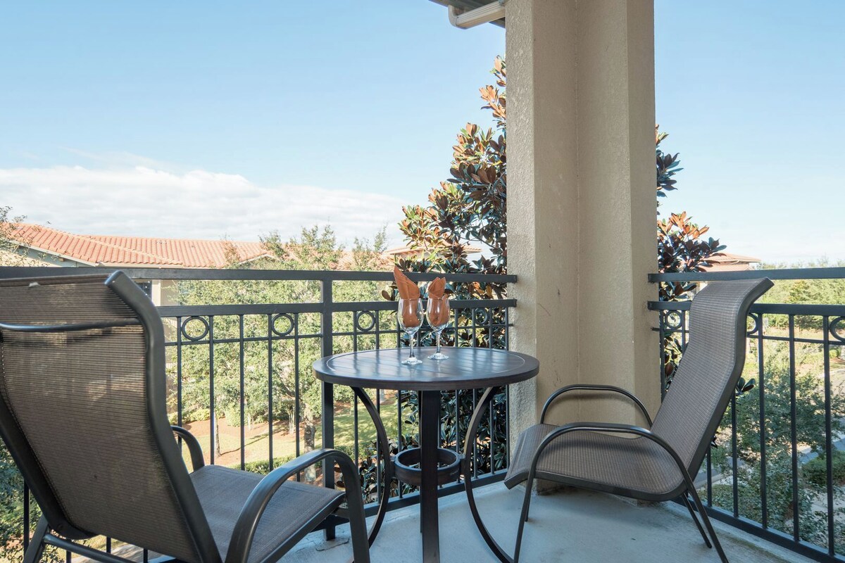 A balcony with a round table, two chairs, and two wine glasses.