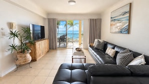 A modern living room with a black leather sofa, a flat-screen TV, a wooden cabinet, and a potted plant. - Villa Vista Three - Superb Ocean View! (Yeppoon)