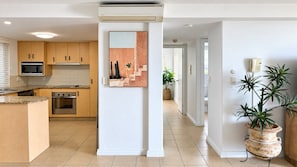 A modern kitchen with wooden cabinets, a built-in microwave, and an oven. There is a painting on the wall and a potted plant in the hallway. - Villa Vista Three - Superb Ocean View! (Yeppoon)