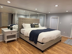 A bedroom with a bed, bedside tables, a mirror, and a wooden floor. - 2 bedroom Hillside Hideaway (Anchorage)
