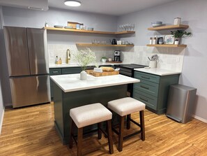 A modern kitchen with a stainless steel refrigerator, wooden bar stools, and a central island. - 2 bedroom Hillside Hideaway (Anchorage)