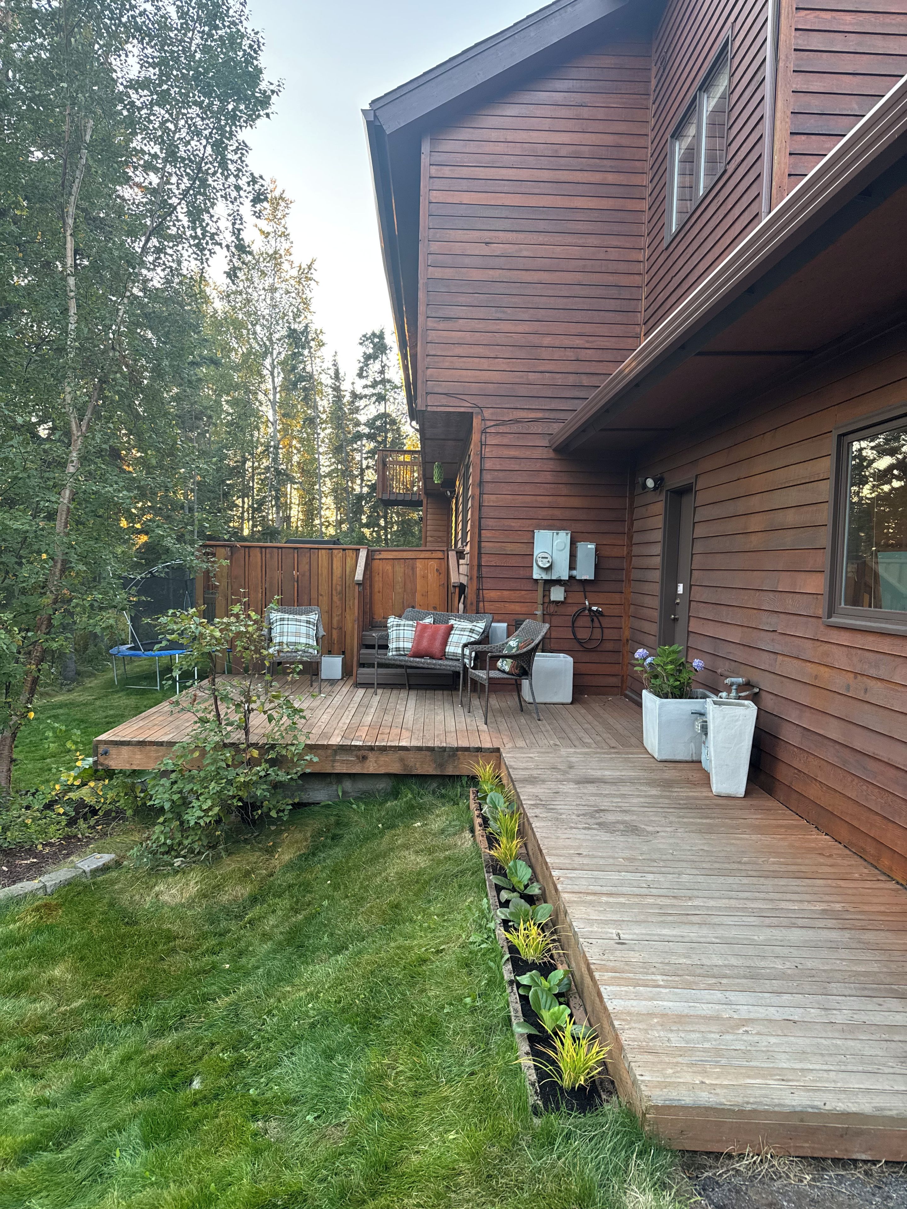 A modern house with a wooden deck, outdoor seating, and a garden area.