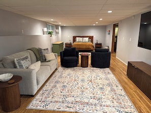 A modern bedroom with a bed, a sofa, two armchairs, a small table, and a TV. - 2 bedroom Hillside Hideaway (Anchorage)