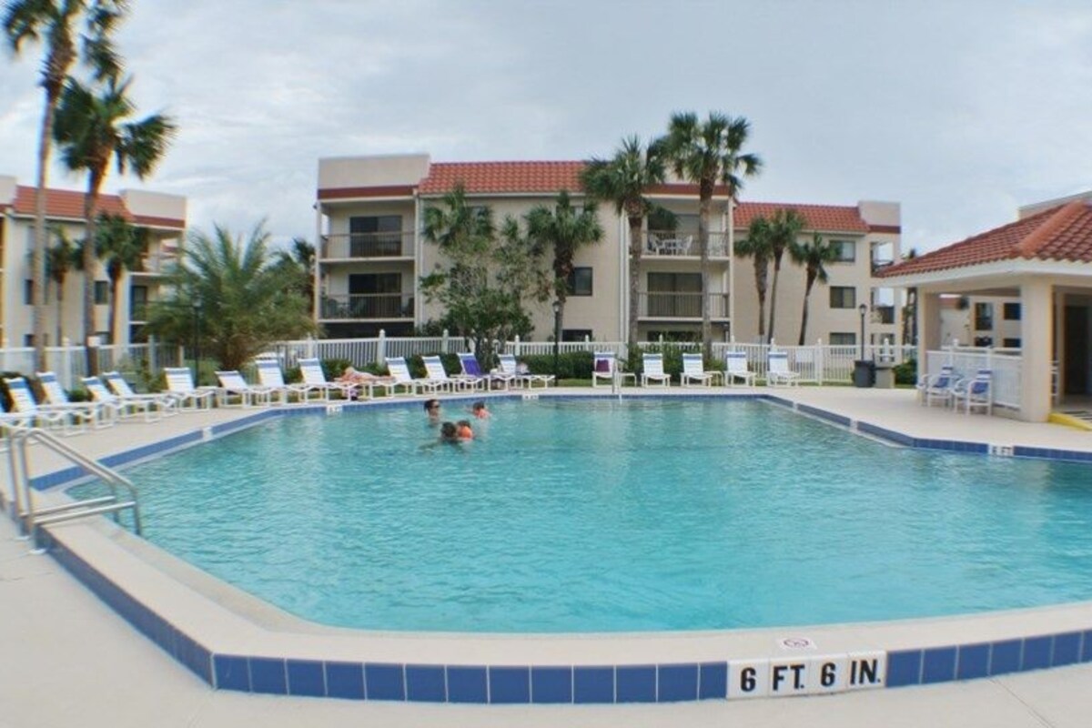 Ein Swimmingpool mit einer Tiefe von 6 Fuß 6 Zoll, umgeben von Liegestühlen und Palmen, mit einem Gebäude im Hintergrund.
