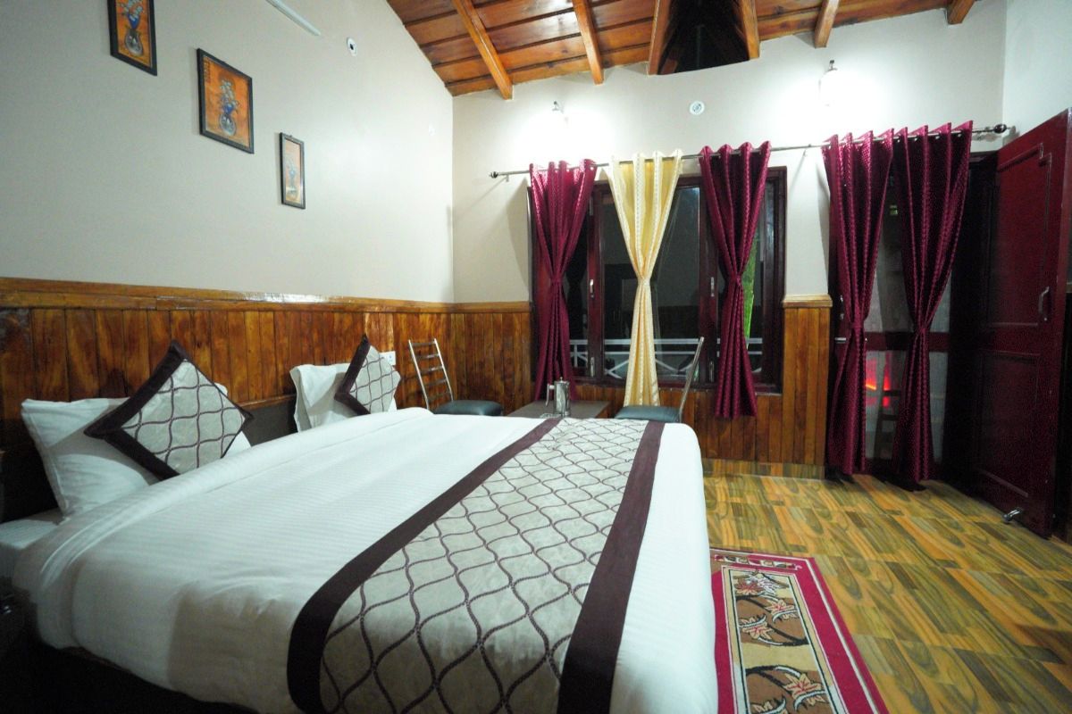 Una habitación de hotel con una cama grande, cabecera de madera, una ventana con cortinas y suelo de madera.