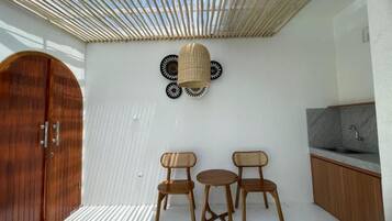 Una habitación con puerta de madera, techo tejido, lámpara de pared y una pequeña cocina con lavamanos.