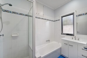 Een badkamer met een douche met glazen wand, een bad, een wastafel met spiegel en witte betegelde wanden.