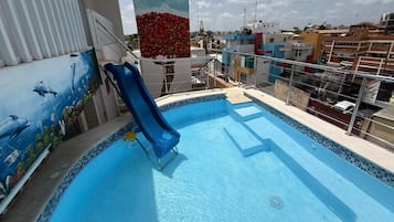 A swimming pool with a slide, surrounded by a poolside area with a railing.