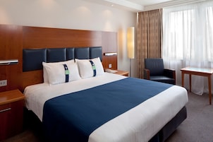 A hotel room with a large bed, a desk, a chair, and a lamp.