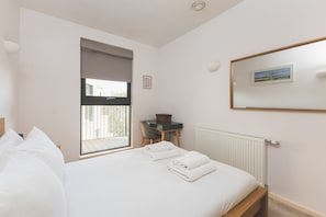 A bedroom with a bed, a desk, a chair, a window, and a radiator. - Stylish Camberwell Two-Bed Retreat (London)