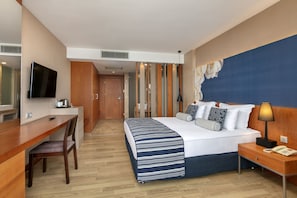 A hotel room with a bed, bedside table, desk, chair, and a television. - Tui Blue Sherwood Belek (Serik)