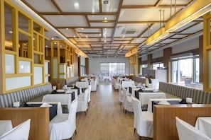 A spacious dining area with multiple tables and booths, wooden paneling on the walls, and large windows providing natural light. - Tui Blue Sherwood Belek (Serik)
