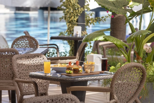 A dining table with a meal, a drink, and a poolside setting with wicker chairs and greenery. - Tui Blue Sherwood Belek (Serik)