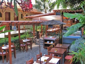 An outdoor dining area with wooden tables and chairs, a covered seating area, and a food stall. - Vila Ventura (Santa Cruz)