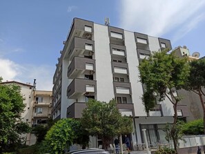 Un edificio residencial de varios pisos con balcones, un acceso con reja y zonas verdes circundantes.