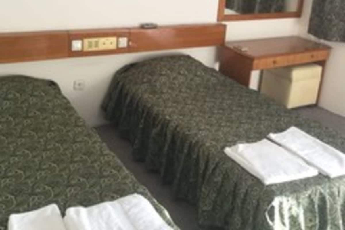 A hotel room with two single beds, a small desk, a mirror, and a wall-mounted light fixture.