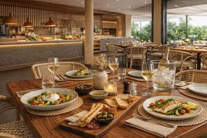 A restaurant setting with tables set for dining, featuring plates of food, glasses of wine, and a variety of condiments. - HD Sensarena (Teguise)
