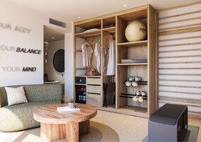 Una sala de estar moderna con una mesa de centro redonda de madera, un sofá y un armario con espejo y ropa colgada.