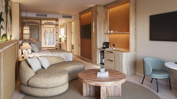 Una habitación de hotel moderna con un amplio sofá modular, una mesa de centro redonda de madera y una zona de estar con una mesita y sillas.