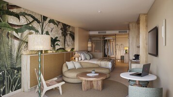 Habitación de hotel con un gran mural tropical, un sofá, una mesa de centro redonda, un televisor y una computadora portátil.