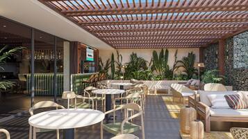 An outdoor seating area with round tables and chairs, a wooden pergola, and lush greenery.