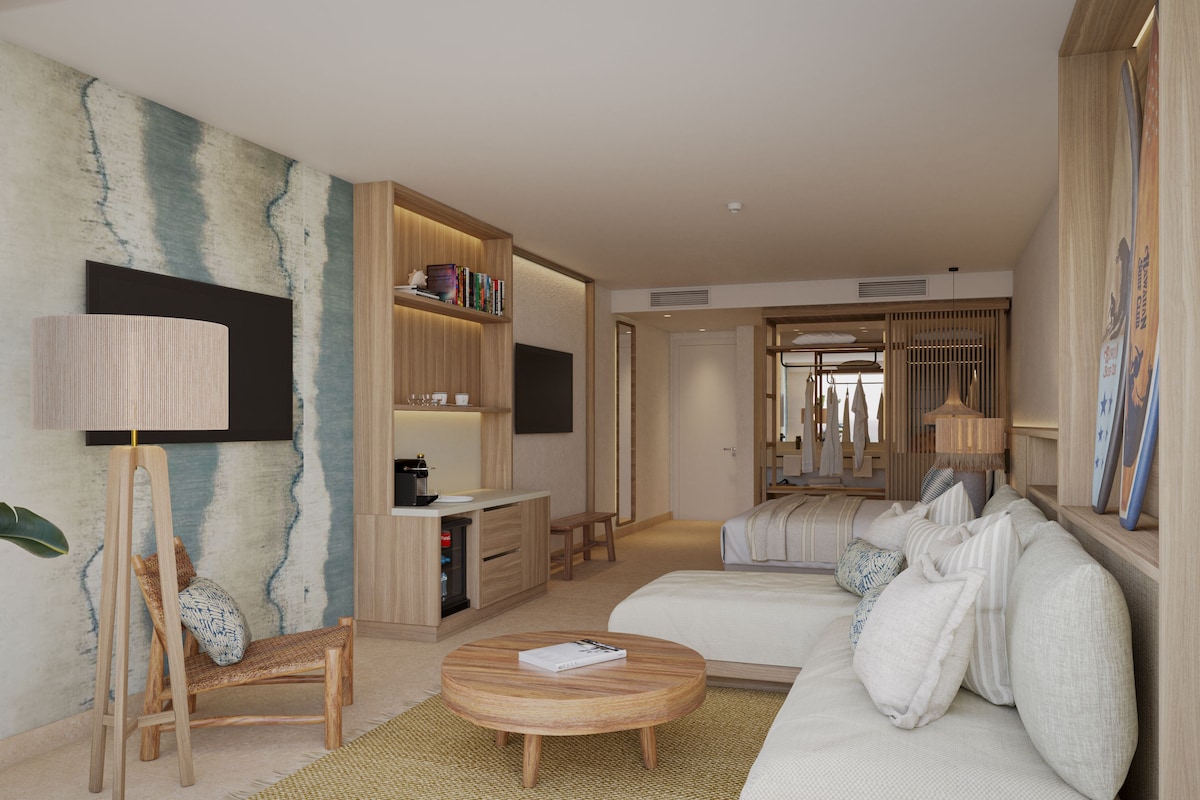 Una habitación de hotel moderna con sofá, mesa de centro, estantería, escritorio y televisor.