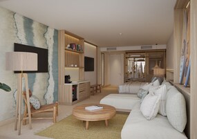 Una habitación de hotel moderna con sofá, mesa de centro, estantería, escritorio y televisor.