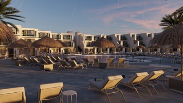 Un resort con piscina, sillas de sol y sombrillas de paja.