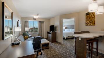 A hotel room with a desk, a chair, a sofa, a TV, a bed, and a bathroom.