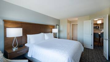 A hotel room with a large bed, two bedside lamps, a nightstand, a chair, and an open door leading to a kitchenette.