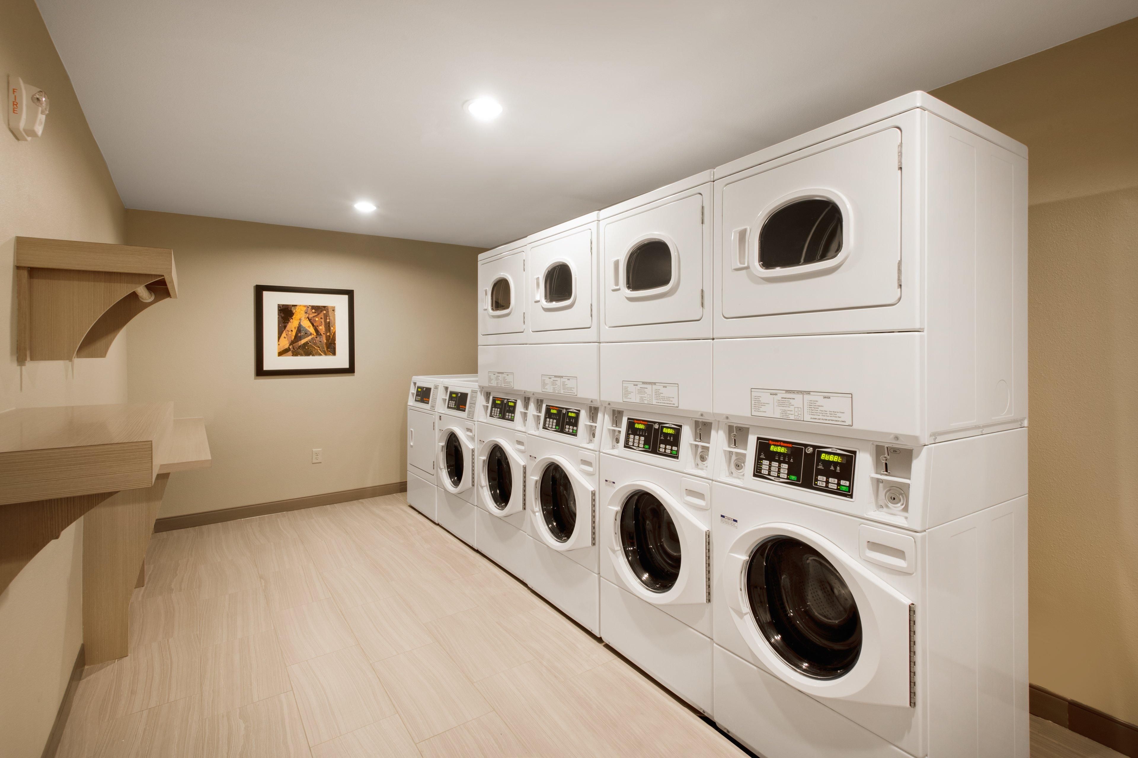 A laundry room with multiple stacked washing machines and dryers, a wooden bench, and a framed picture on the wall.