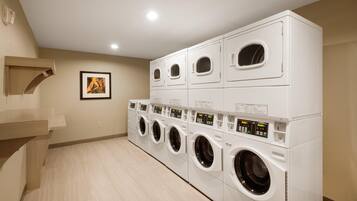 A laundry room with multiple stacked washing machines and dryers, a wooden bench, and a framed picture on the wall.