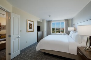 Una habitación de hotel con una cama grande, un escritorio con lámpara, un televisor y una ventana con cortinas.