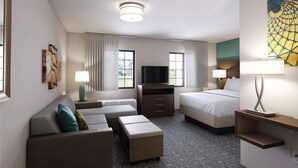 Quarto de hotel com sofá, cama, televisão, secretária e candeeiro.
