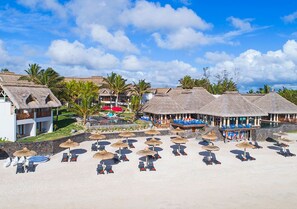 Un resort con edificios de techo de paja, un área de piscina y varias tumbonas con sombrillas.