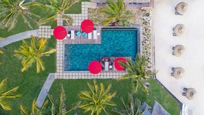 Vista aérea de un resort con piscina, sillas de descanso y palmeras.