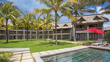 Un resort con piscina, palmeras y un edificio de techo de paja.