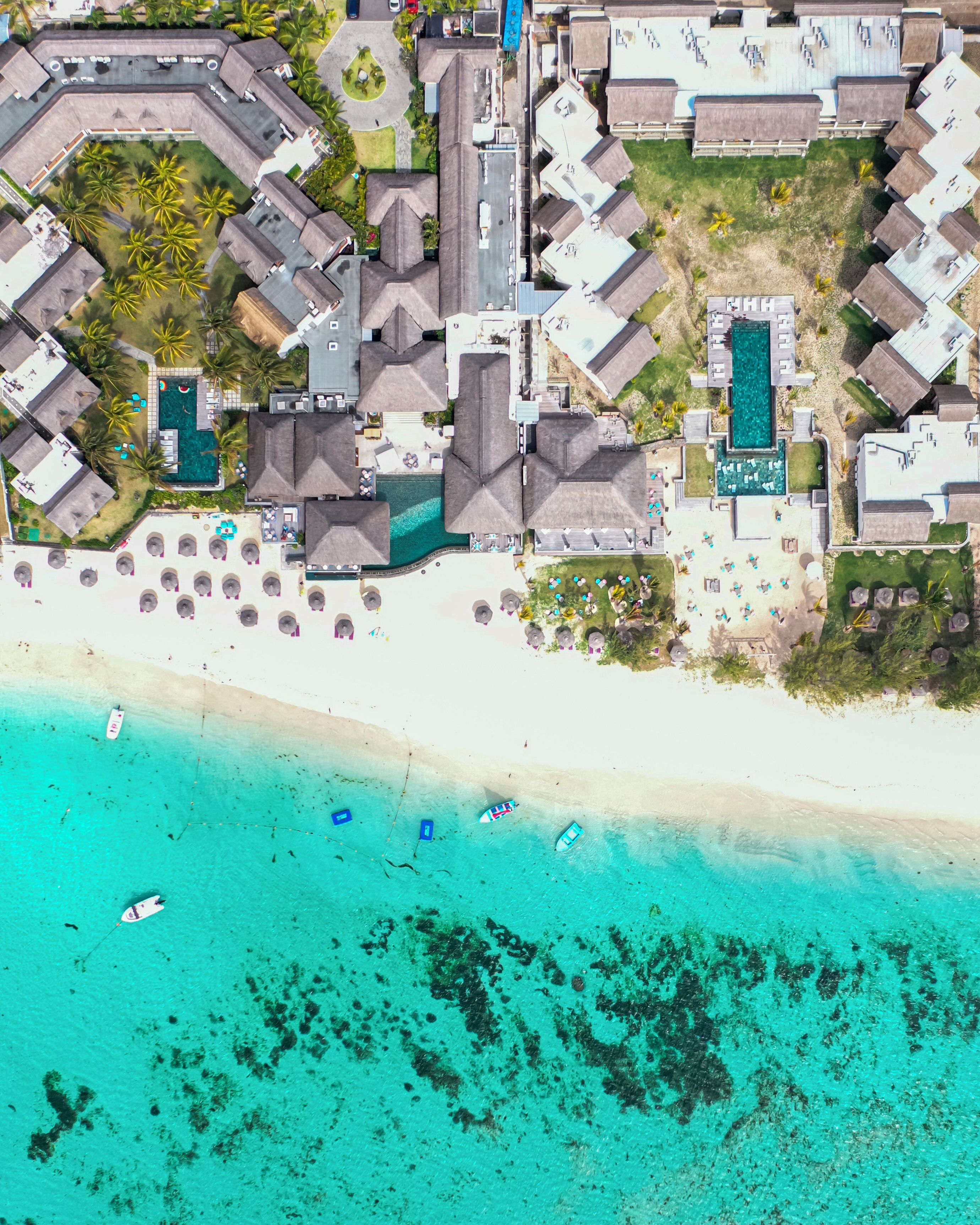 An aerial view of a resort with multiple buildings, a beach, and a clear blue sea.