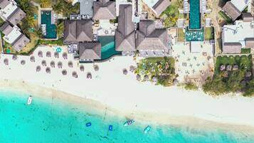 An aerial view of a resort with multiple buildings, a beach, and a clear blue sea.