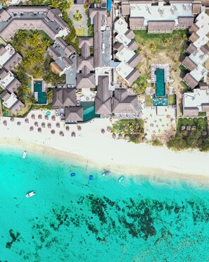 Vista aérea de un complejo turístico con varias edificaciones, una playa y un mar azul cristalino.