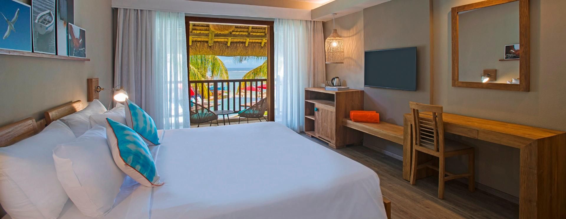 Une chambre d’hôtel équipée d’un lit, d’un bureau, d’une chaise, d’une télévision et d’un balcon donnant sur la piscine.