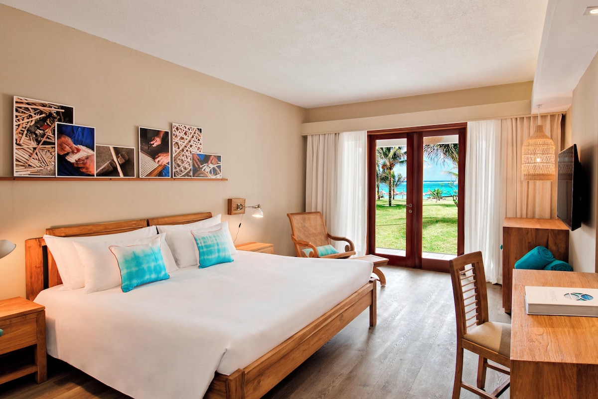 Habitación de hotel con una cama grande, un escritorio con silla, televisión y vista al océano a través de la ventana.