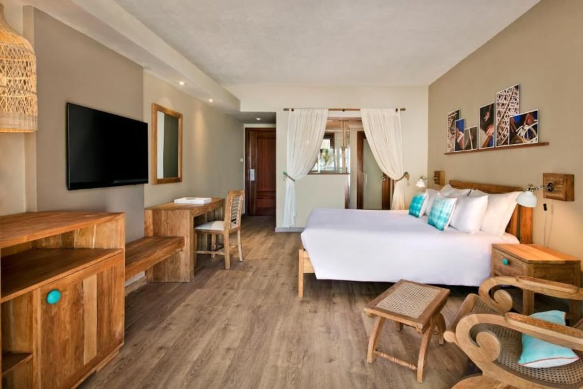 Habitación de hotel con cama, muebles de madera, televisión y obras de arte en la pared.