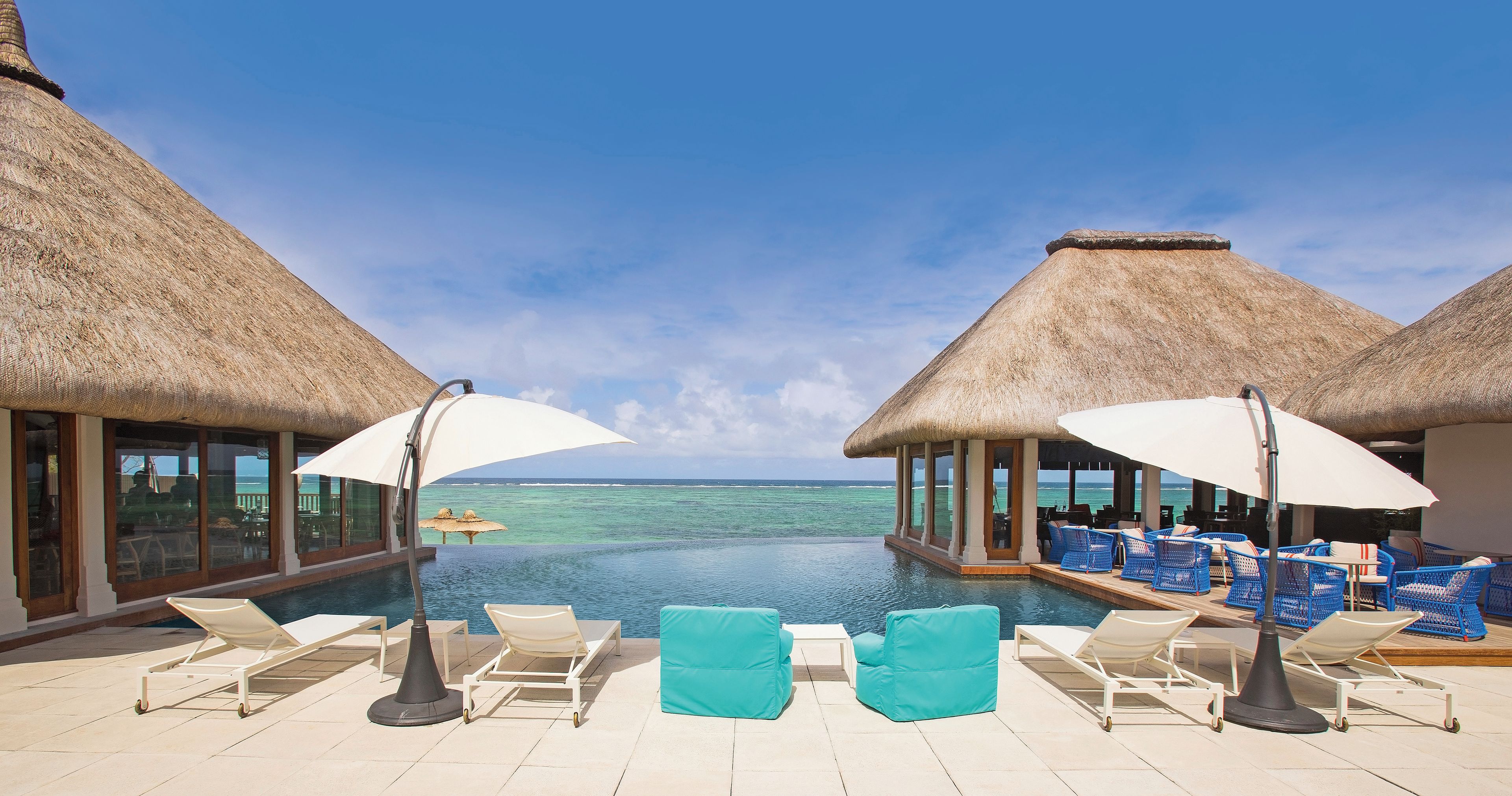 A poolside area with lounge chairs and umbrellas, overlooking a clear blue sea.