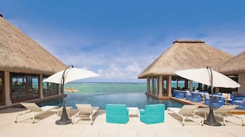 A poolside area with lounge chairs and umbrellas, overlooking a clear blue sea.