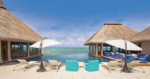 Zona junto a la piscina con sillones de descanso y sombrillas, con vista al mar azul y transparente.