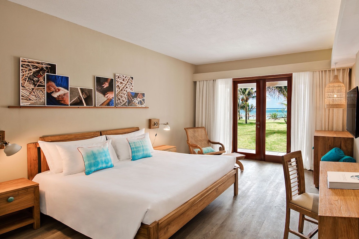 Habitación de hotel con una cama grande, un escritorio de madera, una silla, un televisor y vista al océano por la ventana.