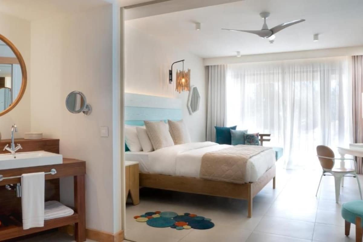 Una habitación de hotel con una cama de madera, un espejo redondo, un lavabo y un ventilador de techo.
