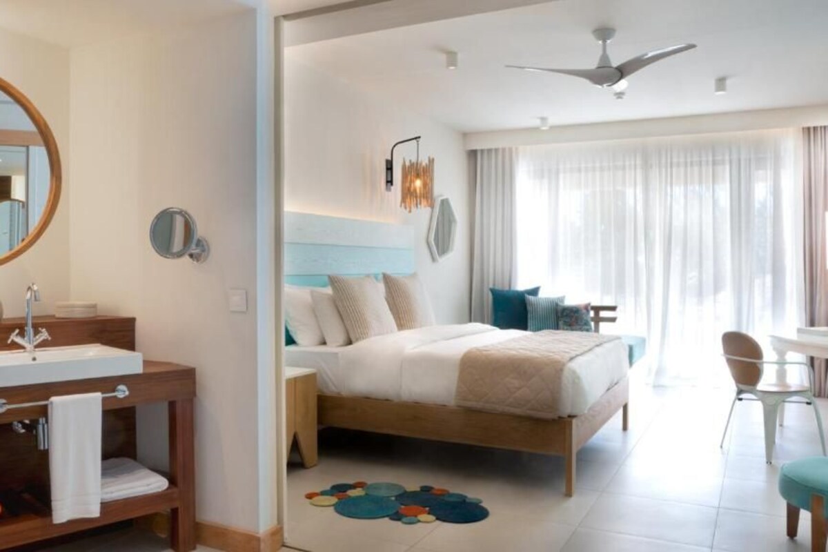 Una habitación de hotel con una cama de madera, un espejo redondo, un lavabo y un ventilador de techo.