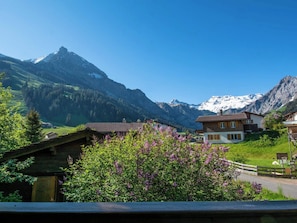 Ein Bergdorf mit traditionellen Holzhäusern, blauem Himmel und schneebedeckten Gipfeln im Hintergrund.